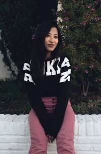 Portrait of happy young woman sitting on retaining wall