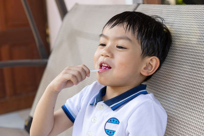 Cute boy eating candy while sitting on chair