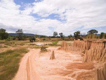 Dirt road passing through landscape against sky