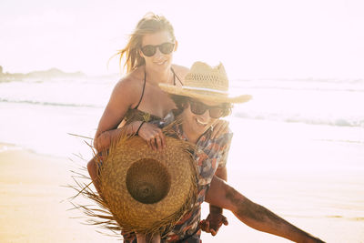 Man piggybacking woman at beach against sky