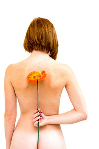 Rear view of shirtless woman holding flower while standing against white background