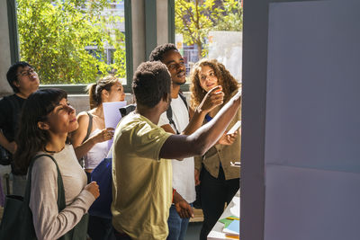 Multiracial male and female students searching on bulletin board in college campus