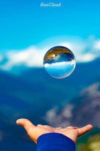 Close-up of hand holding bubbles against blue sky