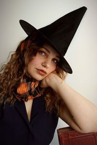 Portrait of young woman wearing witch costume against wall