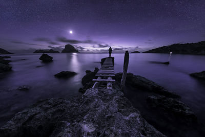Woman standing on pier over sea at night