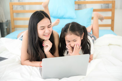 Woman using mobile phone while relaxing on bed