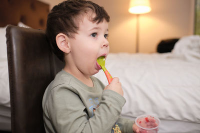 Cute expressive young boy is eating a gelatin snack while watcching tv in a hotel room