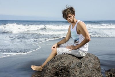 Portrait of young man sitting on rock at beach