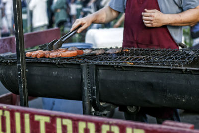 Midsection of man grilling sausages on barbecue