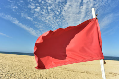 Red flag blowing in wind on flag pole stuck in sand and blue sky background