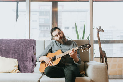 Young man playing guitar on sofa at home