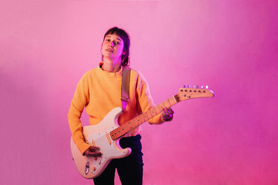 Full length of man playing guitar against pink wall