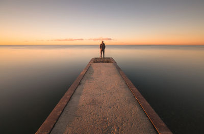Man standing on jetty against sky during sunset
