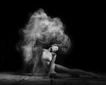 Woman tossing hair while sitting against black background