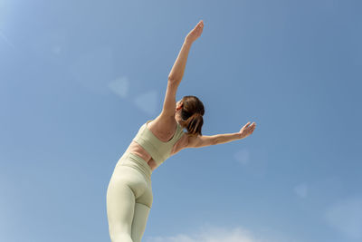 Rear view of a sporty woman with her arms raised in success, against a blue sky.