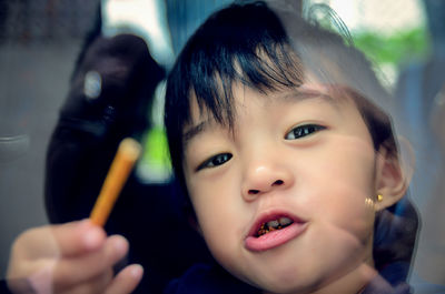 Close-up portrait of boy holding snack seen through glass