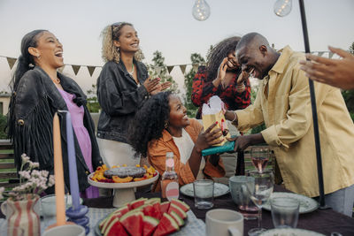 Young man giving gifts to female friend while celebrating birthday in back yard