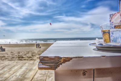 Close-up of drink on table at beach against sky