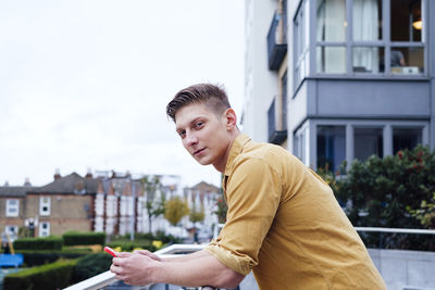 Handsome young man with smart phone leaning on railing