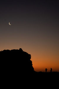 Silhouette man standing on rock at sunset