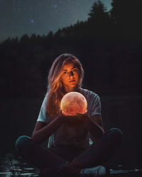 Digital composite image of young woman holding moon against black background