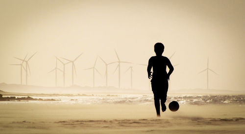 Rear view of silhouette man on beach against sky during sunset