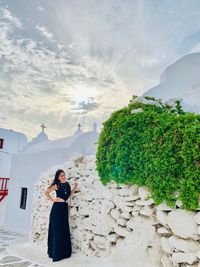 Portrait of woman standing by stone wall against cloudy sky