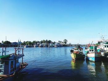 Boats moored at harbor against clear blue sky