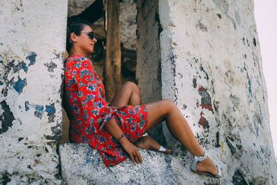 Side view of young woman sitting against wall