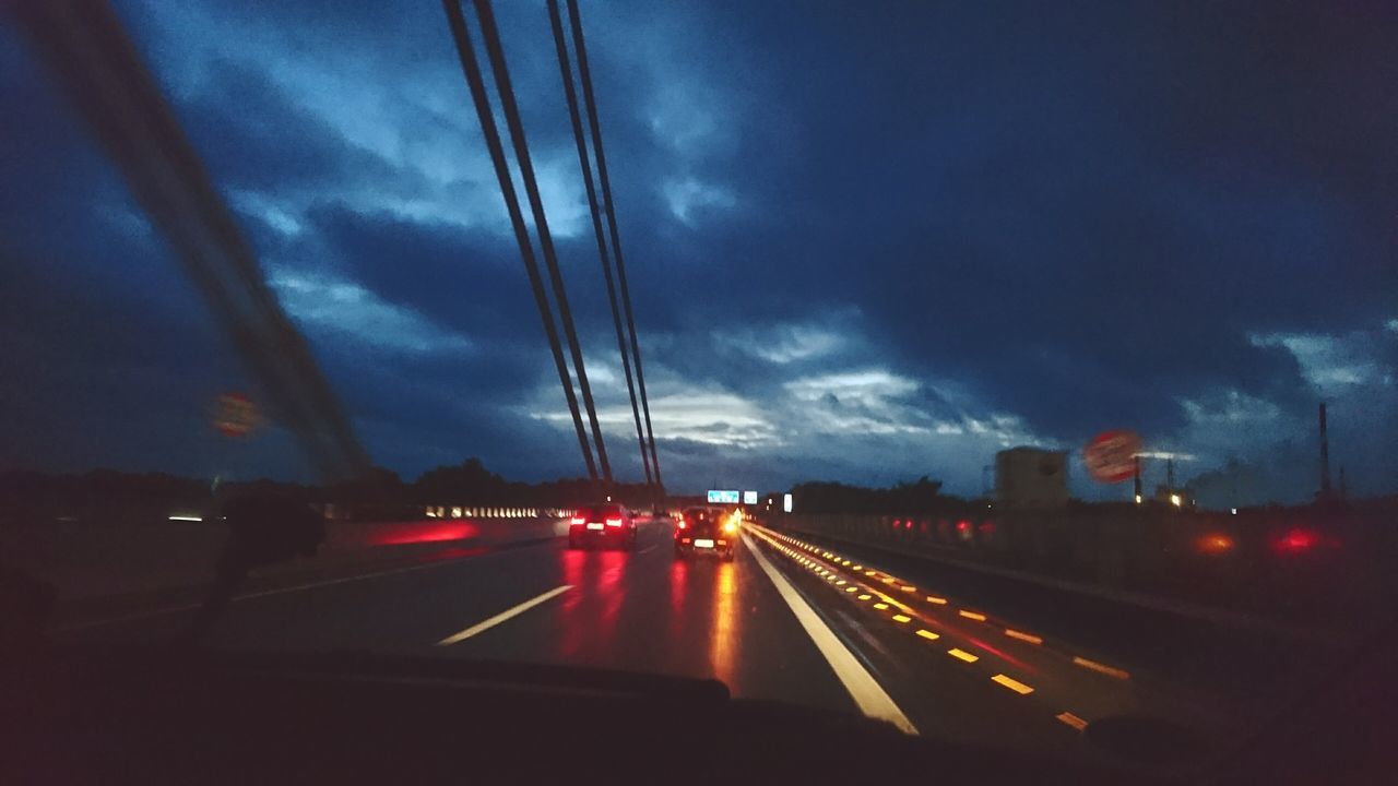 transportation, road, car, illuminated, long exposure, land vehicle, traffic, on the move, motion, mode of transport, blurred motion, sky, night, the way forward, tail light, cloud - sky, city life, diminishing perspective, vanishing point, rush hour, journey, outdoors, engineering, dramatic sky, vibrant color, dividing line