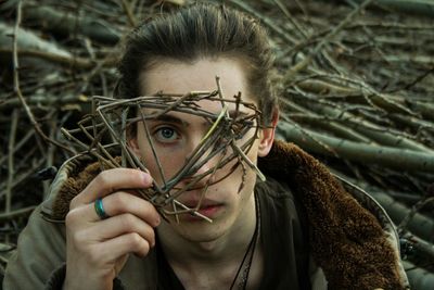 Portrait of man covering face with twigs in forest