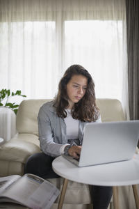 Businesswoman using laptop while sitting on sofa at home