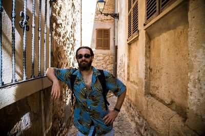 Portrait of young man wearing sunglasses standing at alley