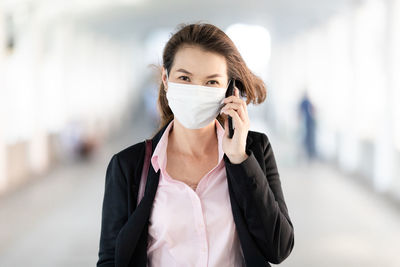 Portrait of businesswoman wearing mask talking on phone while standing outdoors