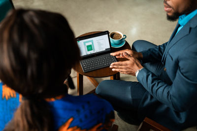 Midsection of businessman wearing suit using laptop having discussion with colleague while sitting at office