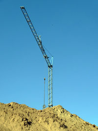 Low angle view of crane against clear blue sky