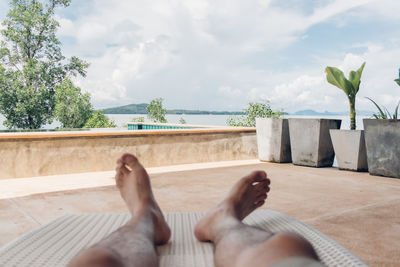 Low section of man relaxing in swimming pool against sky