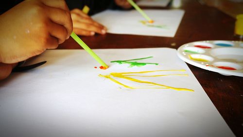 Cropped image of children drawing on paper at table