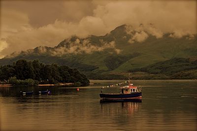 Boat sailing on river by mountains against sky