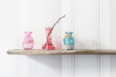 Three pastel colored glass vases with catkins branch stand on old wood