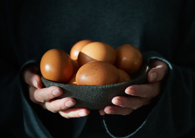 Unusual easter on dark background. bowl of brown eggs with hands. darkness, rays of sunlight