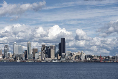 Modern buildings by river against cloudy sky during sunny day