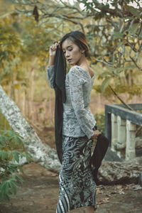 Full length of young woman standing against tree