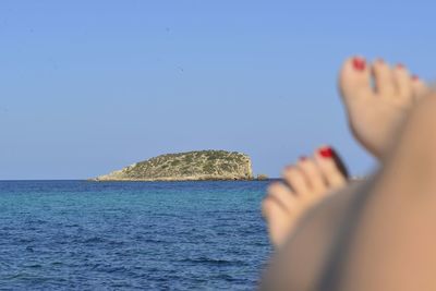 Low section of woman on beach against clear blue sky