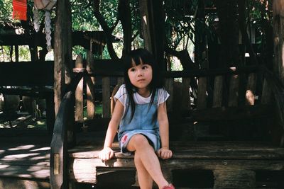 Portrait of girl sitting on wood against trees