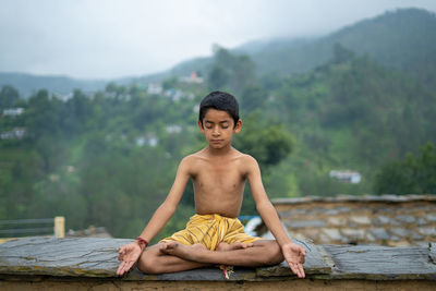 A young indian cute kid doing yoga in the mountains,wearing a dhoti