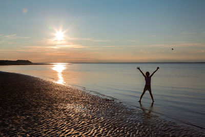 Silhouette girl on shore at beach against sky during sunset