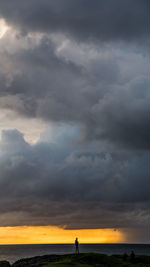 Silhouette person standing on field against storm clouds