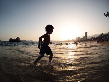 Side view of shirtless boy playing in sea against clear sky