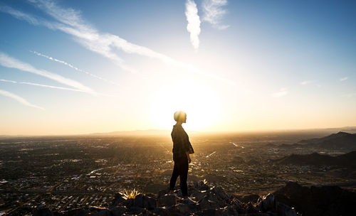 Rear view of woman standing on landscape against sky during sunset